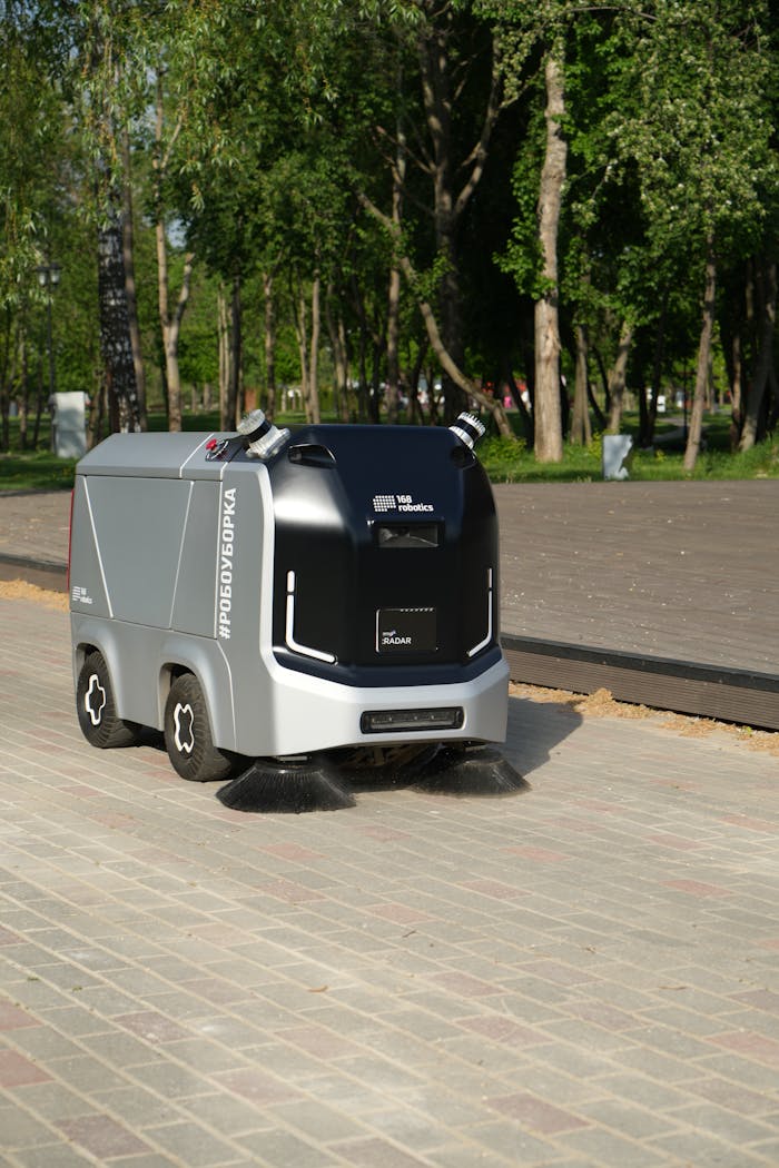 A robotic street sweeper operates autonomously on a city pavement under sunny conditions.