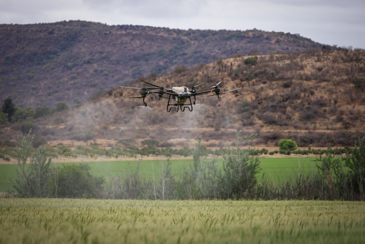 Drone flying over a green farm field with mountains in the background, showcasing agricultural technology.